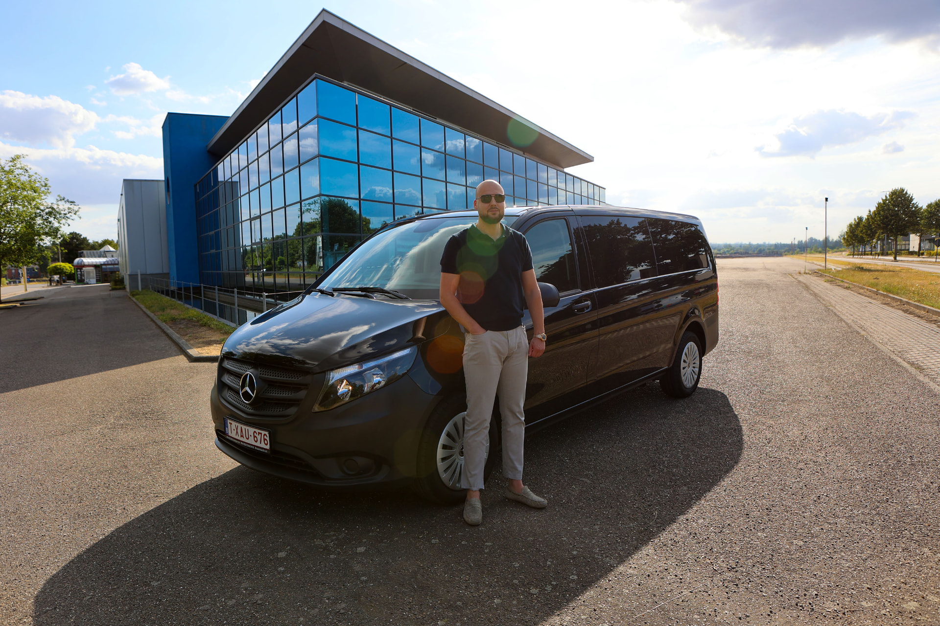 Sander naast zijn zwarte Mercedes Vito voor een modern kantoorgebouw